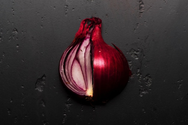 Кусочки красного лука крупным планом Половинки лука помещены на темный текстурный фон Овощ фиолетового цвета, нарезанный на куски Концепция питания и здорового питания