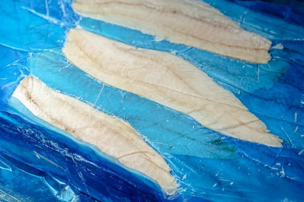 pieces of red and white fish fillet in a package frozen in a cardboard plastic, open, on a dark wood