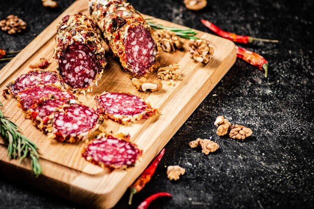 Pieces of salami sausage on a cutting board with pods of dried chili peppers