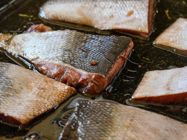 Кусочки лосося с кожей в растительном масле и немного трав на сковороде - для запекания, деталь крупным планом