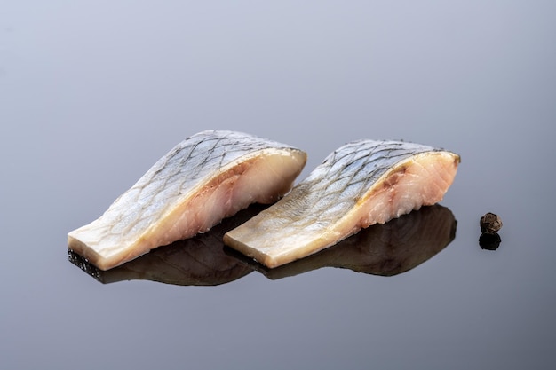 Pieces of salted herring fish on a mirror background