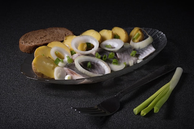 Pieces of salted herring and new rustic potatoes decorated with oniom rings and green onion