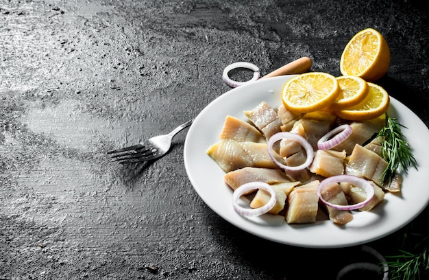 Pieces of salted herring on a plate with sliced lemon and onion