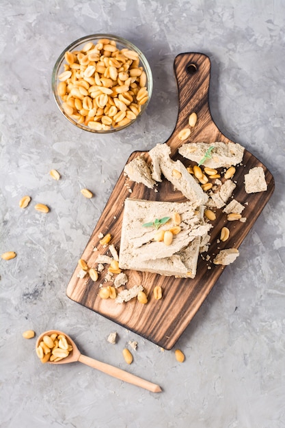 Pieces of sunflower and peanut halva and mint leaves on a cutting board and a bowl of nuts on the table. Caloric oriental dessert. Vertical and top view