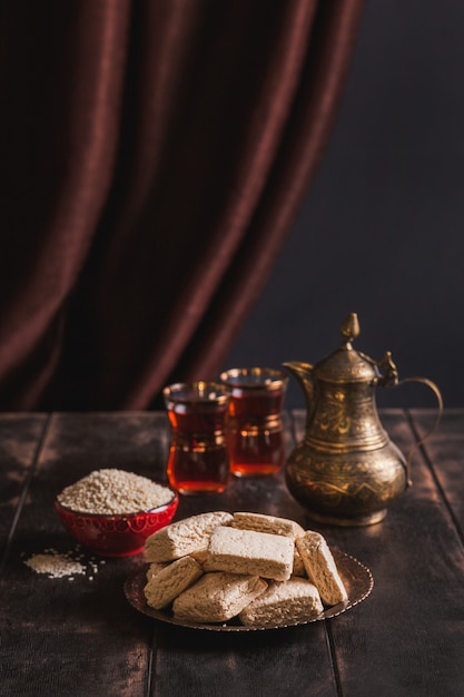 Pieces of tahini halva, sesame seeds in a bowl, tea in Turkish armudas, an vintage jug.