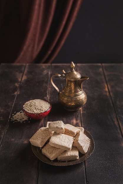Pieces of tahini halva, sesame seeds in a bowl, an vintage jug.. 
