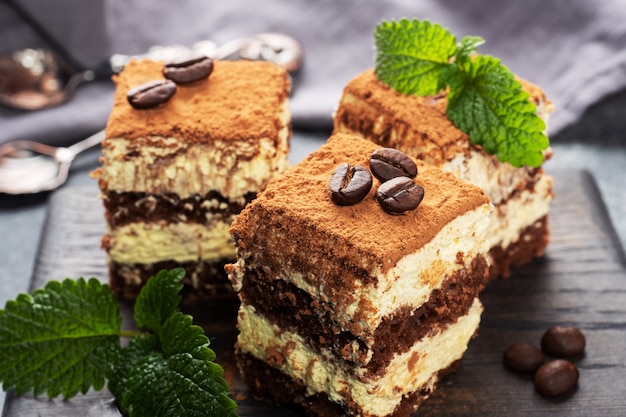 Photo pieces of tiramisu cake with delicate cream, coffee beans and mint leaves.