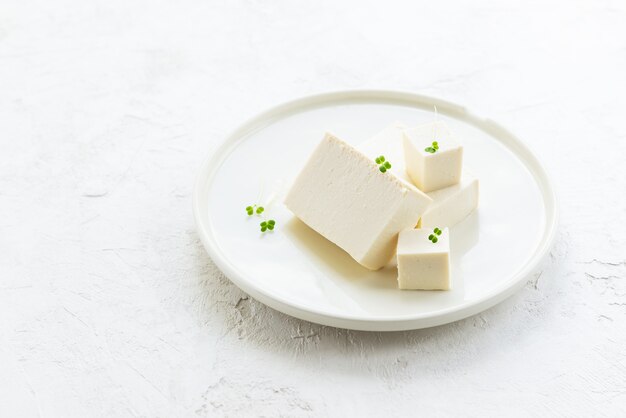 Кусочки сыра тофу с мелкой зеленью на светлой тарелке