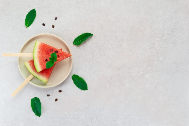 Pieces of watermelon in a wooden stick with mint leaves on a plate