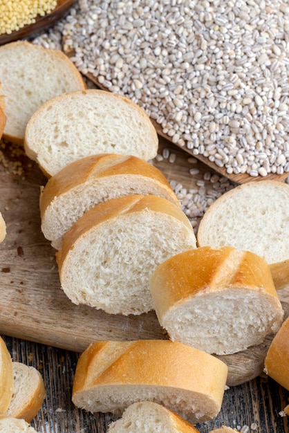 Pieces of wheat baguette on a cutting board pieces of wheat baguette with raw dry cereals and barley