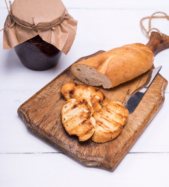 Pieces of white bread on a brown wooden board and raspberry jam