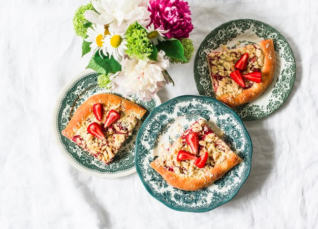 Pieces of yeast dough strawberry rhubarb sweet pie with crumbs on a light background top view