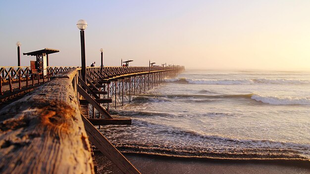 Pier on beach against clear sky during sunset