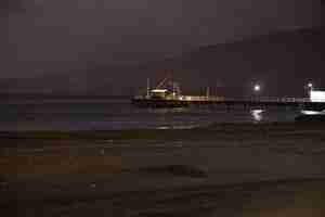 Photo a pier on the beach at night with a mountain in the background.