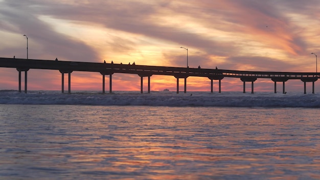 Pier in zeewater op strand oceaan golven hemel bij zonsondergang Californische kust vibes