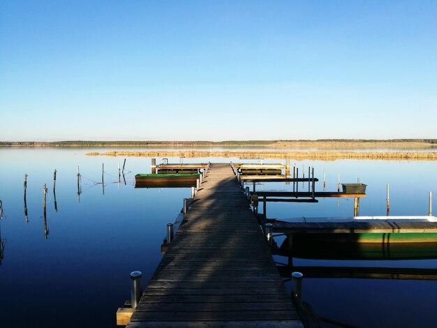 Pier on lake against clear blue sky