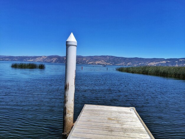 Pier on lake against clear blue sky