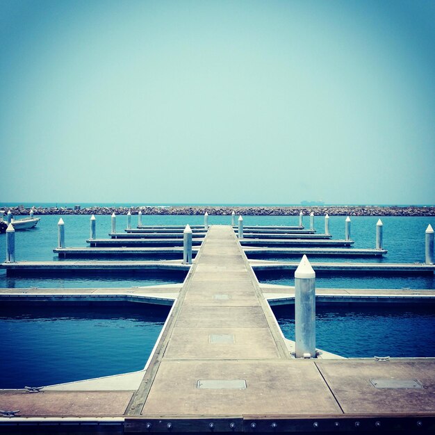 Pier on sea against clear blue sky