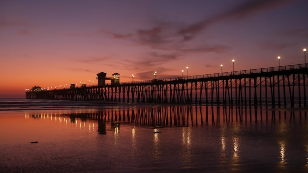 Pier silhouette Oceanside California USA. Ocean tide tropical beach. Summertime gloaming atmosphere.