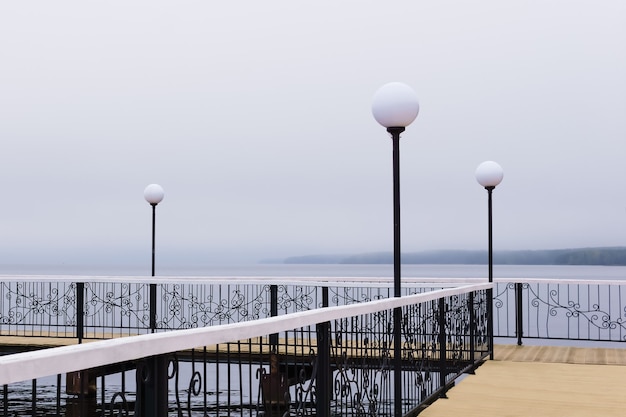 Pier with lanterns on a lake in foggy weather