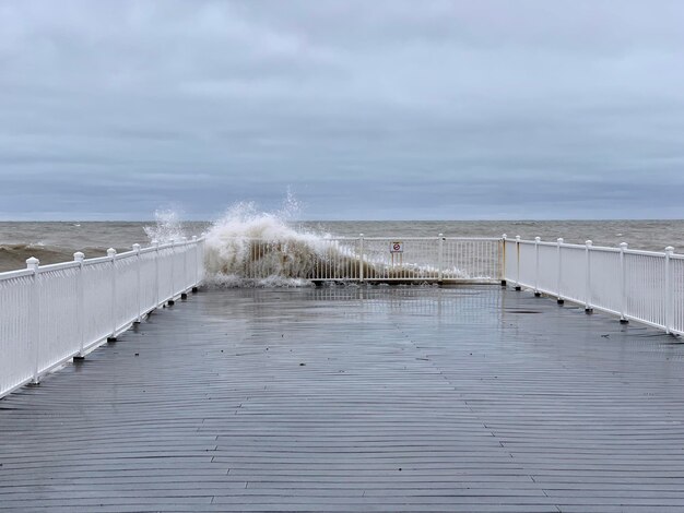 A pier with a wave crashing against it and a man in the water behind it