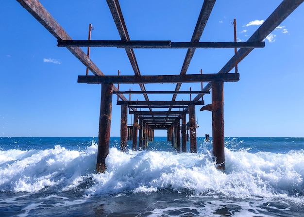 A pier with waves crashing into it and the ocean in the background.