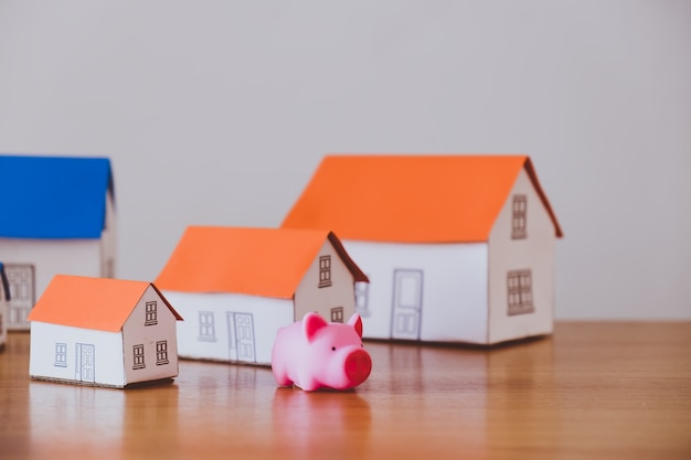 Pig money box and paper house on wooden wall background