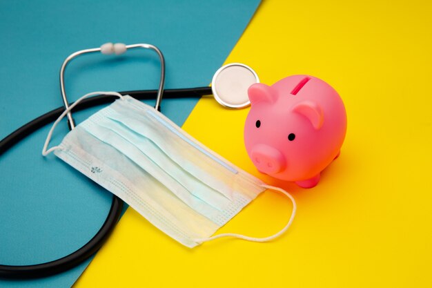 Pig moneybox, face mask and stethoscope on colorful. Spending money on pills and expensiveness of medicine concept.