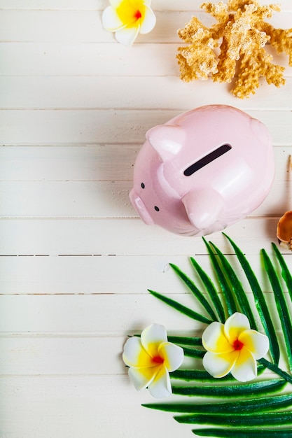 Pig piggy bank, palm leaf and seashells on a wooden background, top view. Concept: saving for vacation.