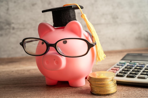 Pigging bank wearing eyeglass with coin calculator and\
graduation hat saving bank education concept