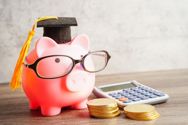 Photo pigging bank wearing eyeglass with coins and calculator saving bank education concept