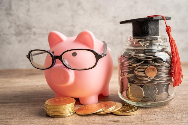 Pigging bank wearing eyeglass with coins and graduation hat saving bank education concept