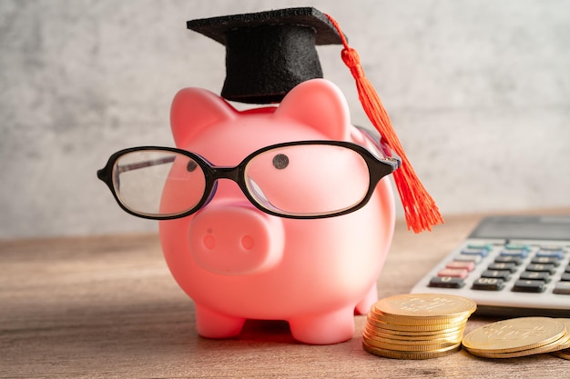 Pigging bank wearing eyeglass with coins and graduation hat saving bank education concept