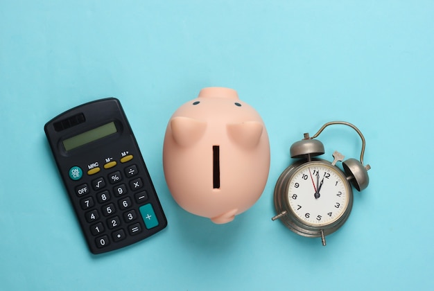 Piggy bank and alarm clock, calculator on blue