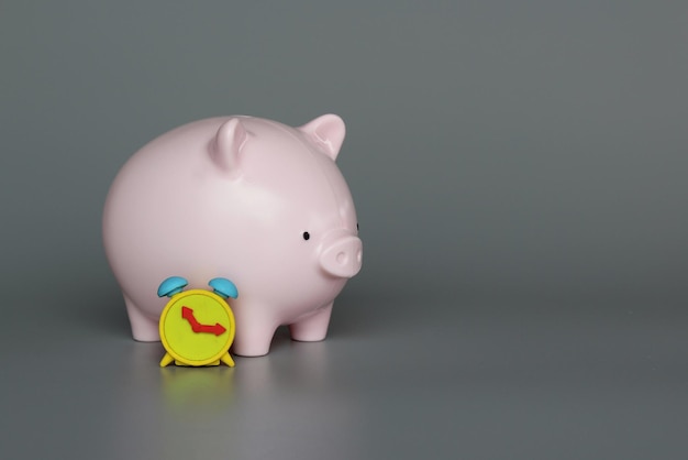 Piggy bank and alarm clock on grey background with copy space Invest inflation savings concept