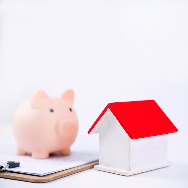 Piggy bank beautiful wooden house model over a signed contract on white background concept of saving money to buy a home insurance close up copy space