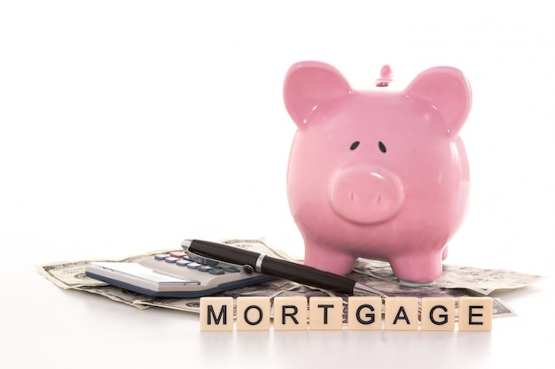 Piggy bank beside calculator and mortgage spelled out in plastic letter pieces