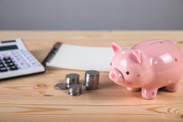 Piggy bank, calculator and coins on wooden surface