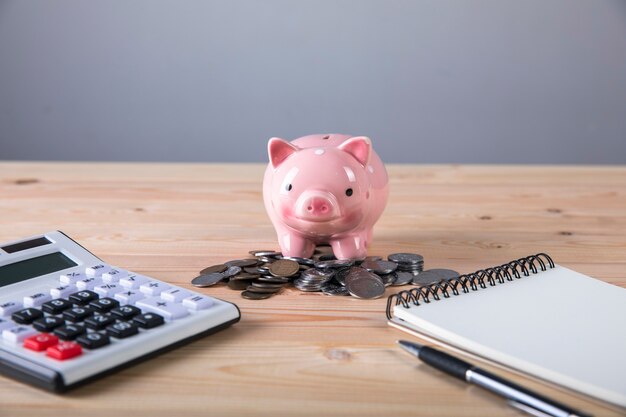 Piggy bank, calculator and coins on wooden surface