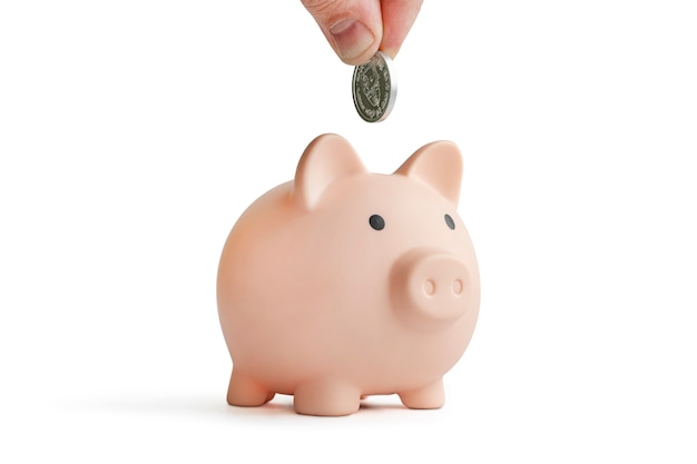 Photo piggy bank for the coin isolated on white background. hand with coin over a piggy bank on white background.