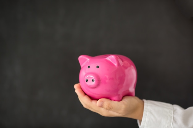 Piggy bank in hand against blackboard blank