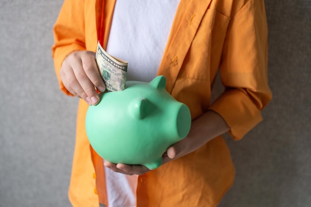 A piggy bank in the hands of a boy in a shirt Put a banknote in a piggy bank