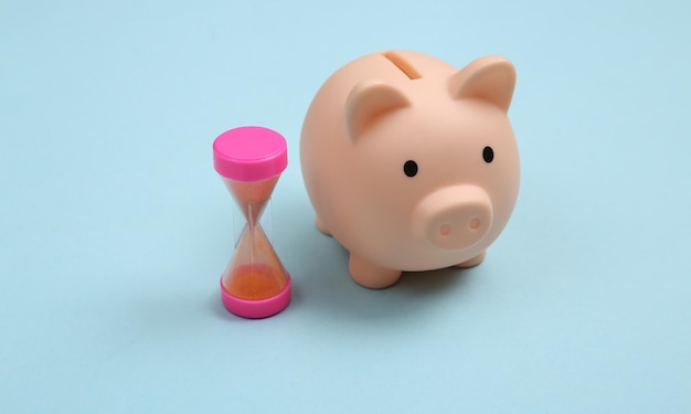 Piggy bank and hourglass on blue background deposit investments\
concept