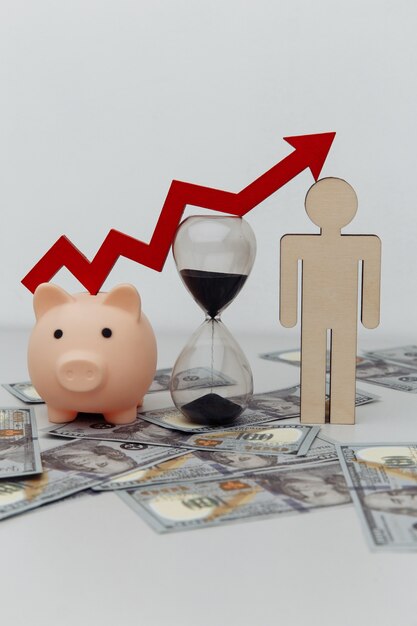 Piggy bank, hourglass and wooden person with arrow up on dollar\
banknotes close-up. investment and time concept.