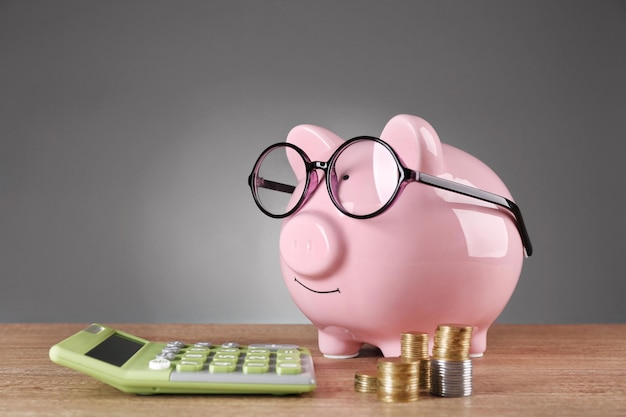 Piggy bank in glazen met rekenmachine en munten op grijze achtergrond