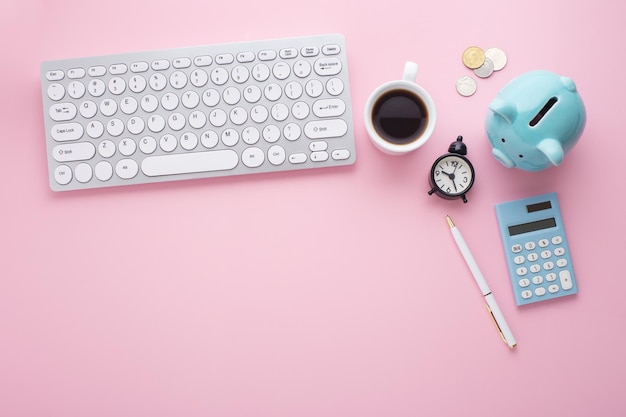 Piggy bank keyboard clock calculator and coins on pink desk