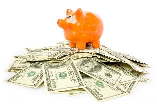 Piggy bank lies on a pile of dollars isolated on white