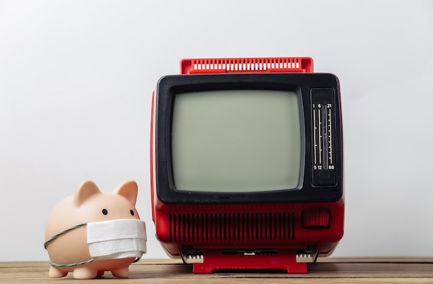 Piggy bank in a medical mask with a retro TV on a white background. Media information about covid-19