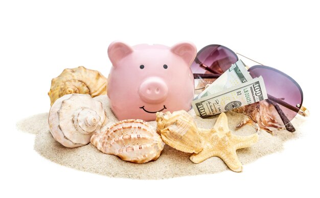 Piggy bank met schelpen zonnebrillen en geld op stapel zand geïsoleerd op wit Besparingen voor vakanties