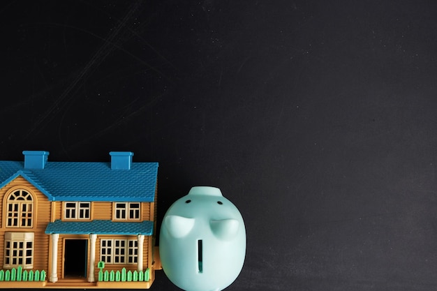 Piggy bank and model house against blackboard